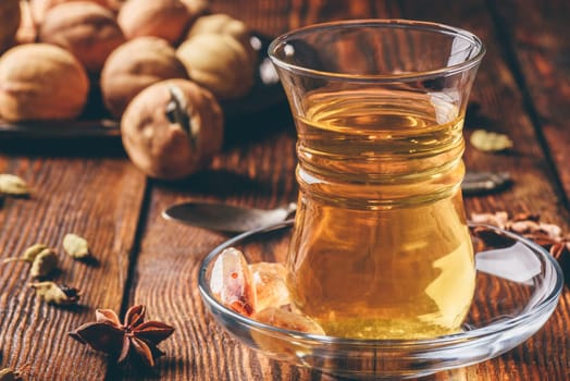 Spiced tea with star anise, cardamom and dried lime in oriental glass over wooden surface