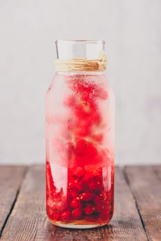 Red currant infused water with ice in glass bottle