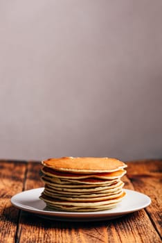 Stack of american pancakes on white plate over wooden table