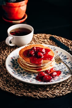 Stack of pancakes with dogberry jam on white plate with ornate