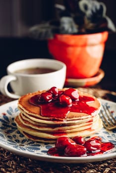 Stack of pancakes with cornelian cherry jam on white plate with ornate
