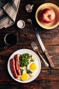 Breakfast with fried eggs, sausages and green peas on white plate