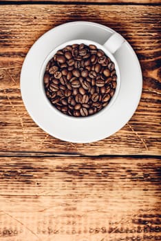 Cup full of roasted coffee beans on saucer over wooden table