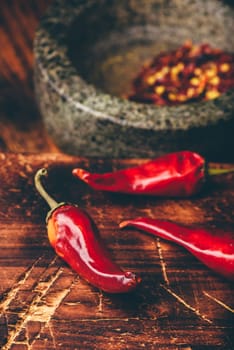 Sun dried red chili peppers on wooden surface with mortar and pestle