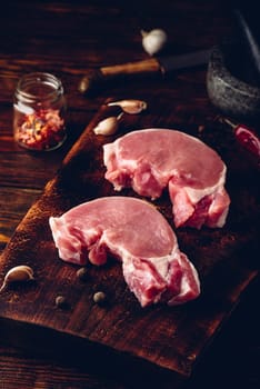 Two raw pork loin steaks on chopping board