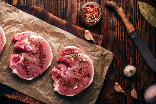 Raw pork loin steaks with different spices on baking paper