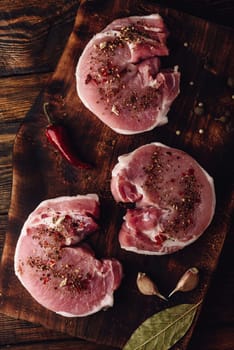 Raw pork loin steaks with different spices on rustic cutting board