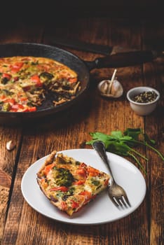 Vegetable frittata with broccoli, red bell pepper and red onion on white plate and in a cast iron