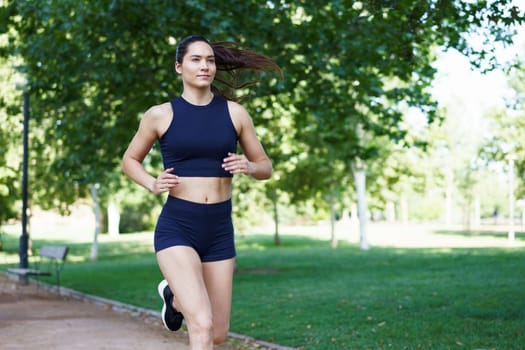 A young woman in athletic wear is jogging in a sunny park, representing fitness, health, and wellness outdoors. The energy and vitality in the scene demonstrate a commitment to an active lifestyle