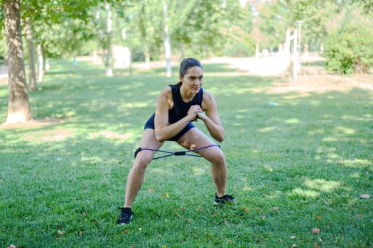 In a serene park setting, a woman showcases her dedication to wellbeing by incorporating resistance band squats into her workout routine, seamlessly blending fitness with the beauty of nature