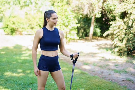 In a sunny park surrounded by lush greenery, a person in navy blue activewear focuses on fitness using resistance bands. Radiating health, fitness, and motivation, they inspire others around