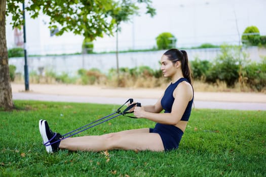 A woman in activewear showcases fitness with resistance bands in a serene park, promoting a healthy lifestyle and wellbeing. Her dynamic movements inspire leisure in nature for wellness