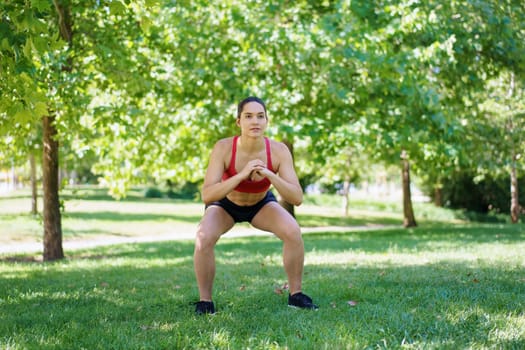 A woman in sportswear is squatting in a sunny park, promoting outdoor fitness, strength training, and a healthy lifestyle for her wellbeing. She highlights active living and dedication to exercise