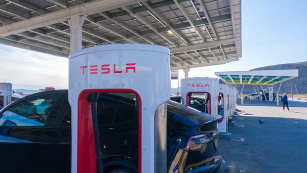 Baker, California, USA-December 3, 2022-During the day, a Tesla vehicle is seen charging at a Tesla Supercharging station, utilizing the high-speed charging infrastructure for convenient and efficient electric vehicle refueling.