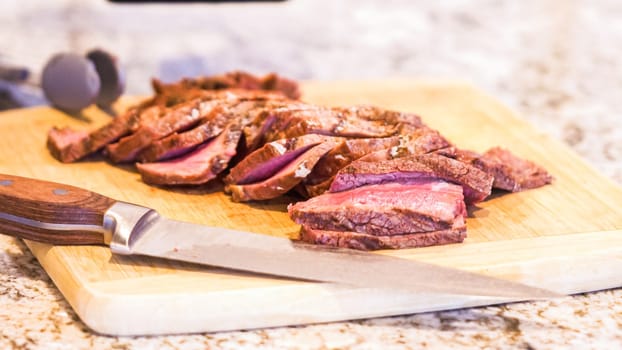 Gloved chef slices succulent pink steak on natural bamboo board, kitchen backdrop.