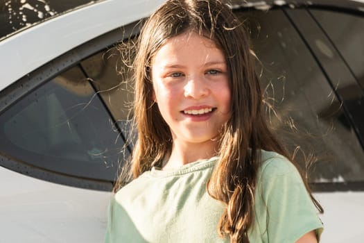 A young girl enthusiastically assists in washing the family's electric car in their suburban driveway.