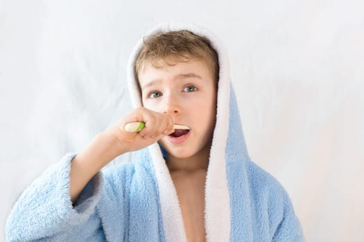 small child, boy in a blue terry robe with a toothbrush on white. A child brushes his teeth. Healthcare and dental care.