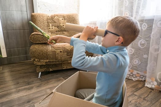 Playful cheerful child, boy looking into a cardboard tube, sitting in a box.