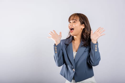 Portrait of a successful Asian business woman wearing a suit in a cheerful profile, raising her fists with a smile. Studio shot isolated on white, expressing triumph and excitement