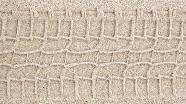 A serene image captures a single tire track delicately etched on the sandy shore, blending human touch with natures beauty in a harmonious display of contrast and tranquility.