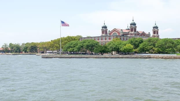 Immigration Museum on Liberty Island with American Flag and New York City Skyline New York NY USA 2023-07-30.