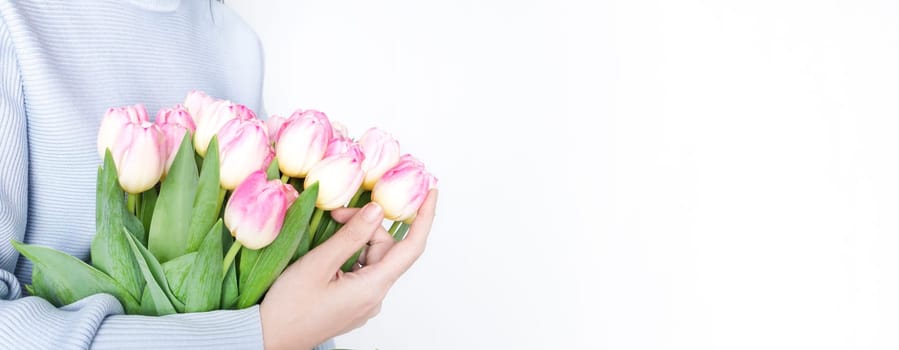 Woman holding a beautiful bouquet of vibrant pink tulips with green foliage against a white background. The pink tulips are striking and complement the womans attire perfectly.