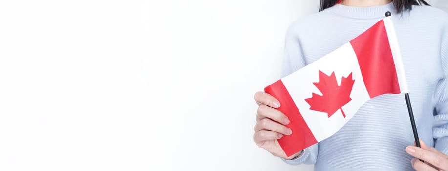 Unrecognized girl student in white blue shirt holding small Canadian flag over gray background, Canada day, holiday, vote, immigration, tax, copy space.