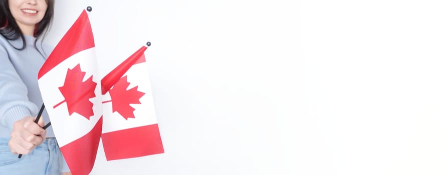 Unrecognized girl student in white blue shirt holding small Canadian flag over gray background, Canada day, holiday, vote, immigration, tax, copy space.