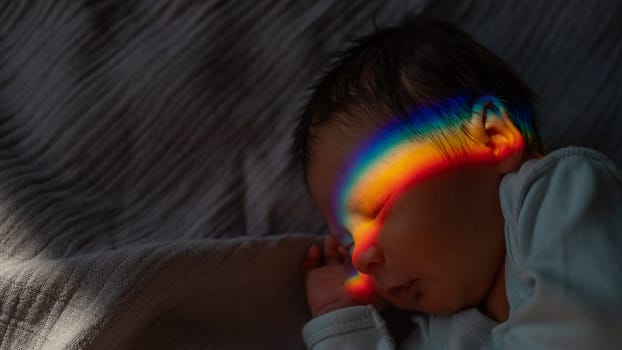 Close-up portrait of a newborn boy with a prism beam on his face. Rainbow