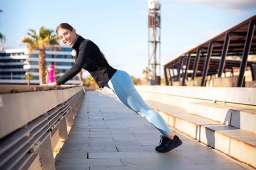 Young sporty woman wearing sportswear headphones doing stretches smiling looking at camera outdoors.