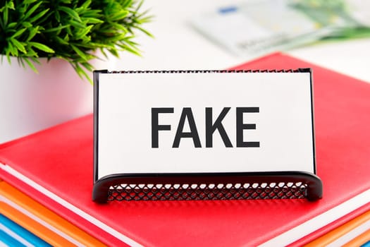 Fake news and digital communication concept. FAKE written on a business card standing in a stand on a notepad