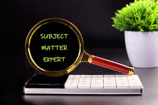 Lifestyle, business finance, education technology concept. Copy space. Text SUBJECT MATTER EXPERT through the lens of a magnifying glass in the dark