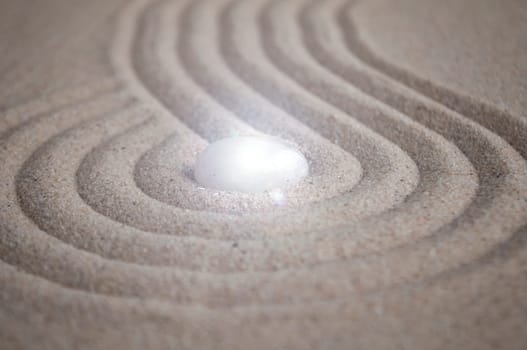 Shining Zen stone in the middle of curve lines on sand.
