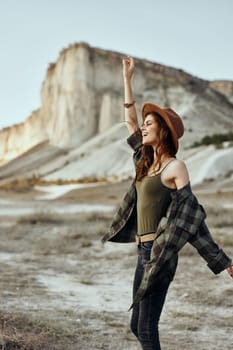 Serene woman in plaid shirt and hat with arms outstretched standing in vast desert landscape