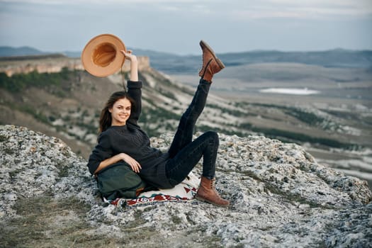 carefree woman in straw hat relaxing on rocky ledge with legs raised in air