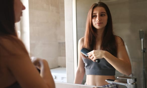 Teenage Girl Combing Her Hair In The Bathroom Mirror In The Morning After Waking Up