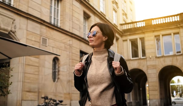 Attractive stylish Woman In Sunglasses Walks By City Street With Backpack