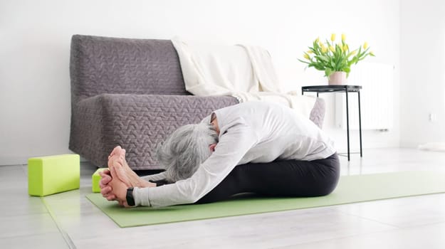 Elderly Active Woman Doing Yoga Fold Pose At Home