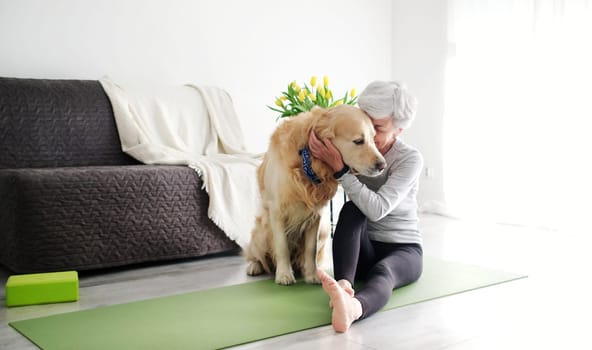 Elderly Woman With A Smile, Actively Hugging Her Dog On A Yoga Mat At Home