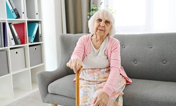 Elderly Woman Sitting On A Living Room Sofa With Cane Laughing And Looking Into The Camera
