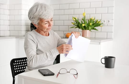 Cheerful Elderly Lady Unwraps Envelope Containing Documents And Papers At Home