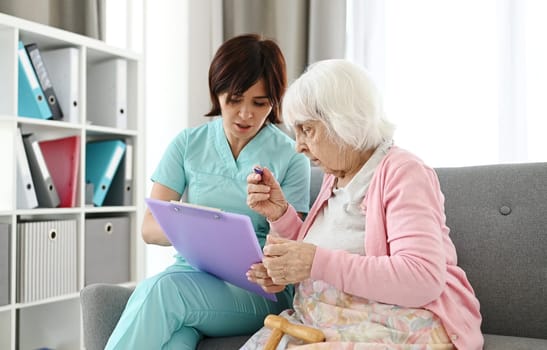 Medical Worker Reads Health Documents To An Elderly Woman In A Bright Room