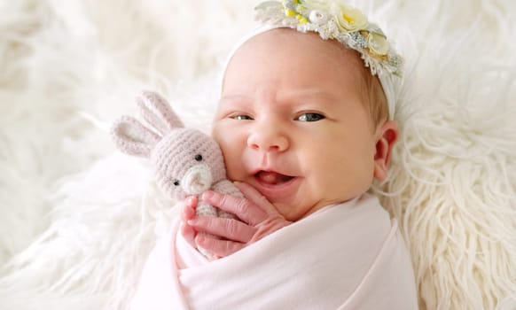 Smiling Newborn Baby Wrapped In A Blanket Holding A Knitted Toy