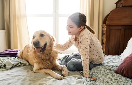 Joyful Little Girl Petting Golden Retriever Dog On A Bed