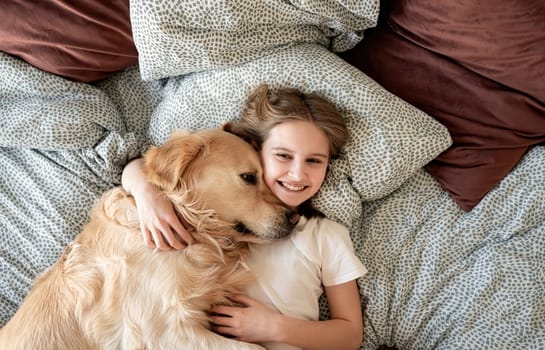 Happy Little Girl Hugging Dog And Smiling Lying On A Bed