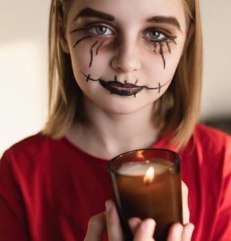 Preteen girl with spooky Halloween makeup posing at camera with lighting candle. Kid's portrait for creepy holiday.