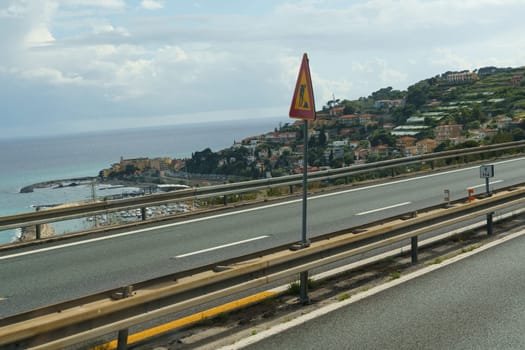 A scenic highway overlooking a harbor and coastline with a warning sign indicating road workers ahead.