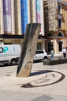 Figueres, Spain - May 13, 2023: A shiny silver sculpture stands in the middle of a city street, reflecting the buildings and people passing by.