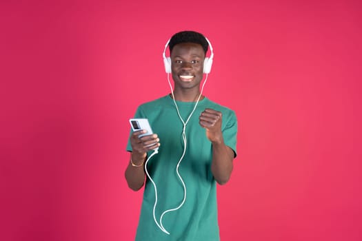 A young man is wearing headphones and holding a cell phone. He is smiling and he is enjoying his music