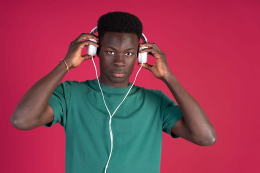 A man wearing a green shirt and headphones. He is looking at the camera. Concept of focus and concentration as the man listens to music